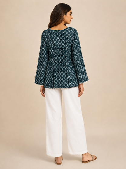 A woman is shown from the back wearing a dark teal long-sleeve kurta with a white floral pattern, paired with white wide-leg trousers and flat sandals, set against a solid beige studio background.