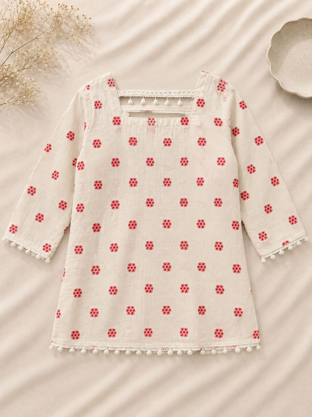Ivory kurta with red floral print and white pom-pom trim displayed in a professional flat lay